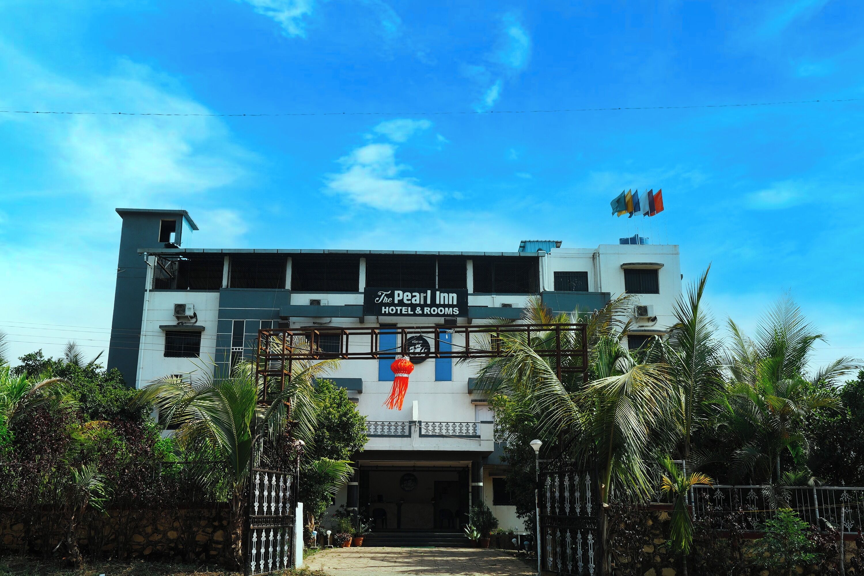 A hotel named 'The Pearl Inn' with a signboard, surrounded by greenery and a clear sky.