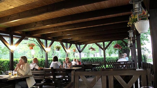 Un espace de restauration en plein air avec des tables et des bancs en bois, entouré de verdure et agrémenté de jardinières suspendues.