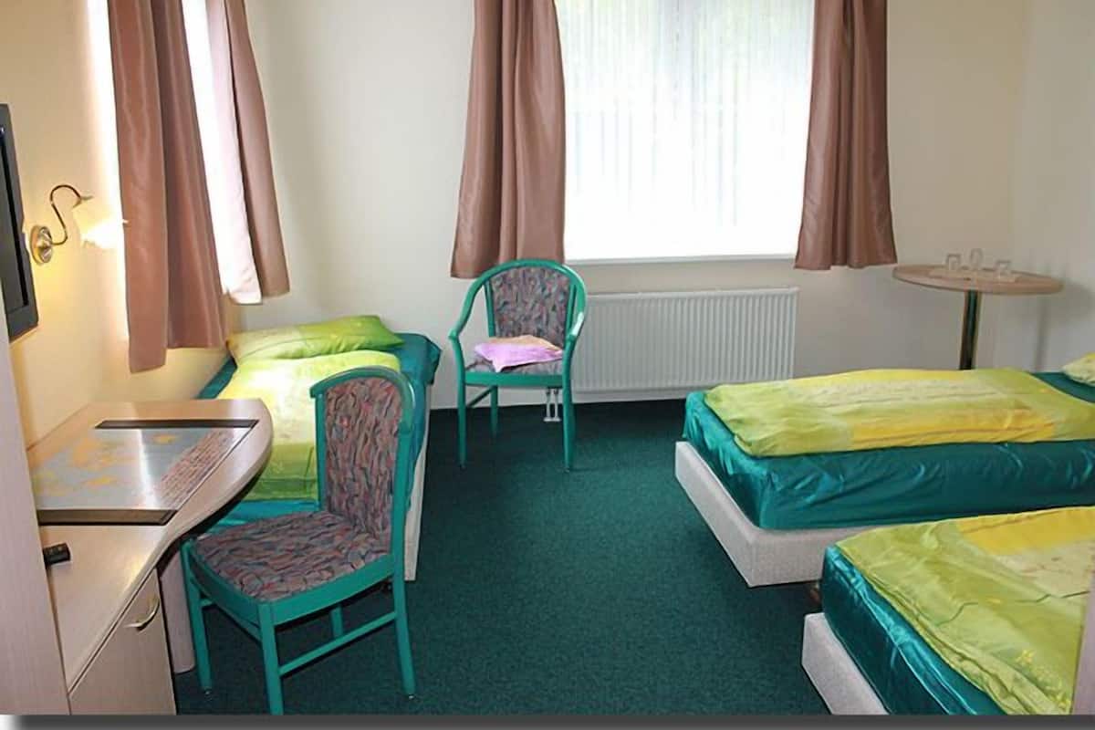 A room with two beds, a chair, a table, and a window with curtains.