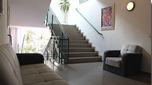 Un salon avec un canapé beige, un fauteuil gris, un escalier avec des rampes vertes et une plante en pot.
