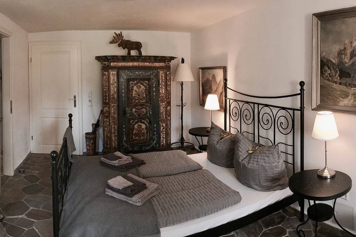 A bedroom with a bed, a dresser, a lamp, and a painting on the wall.