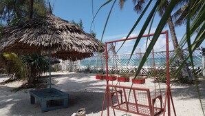 A beach area with a thatched umbrella, a swing set, and a view of the ocean. - Ocean Dream Beach Villa (Dar es Salaam)