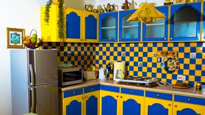 A kitchen with blue and yellow cabinets, a refrigerator, a microwave, and a checkered backsplash. - Ocean Dream Beach Villa (Dar es Salaam)