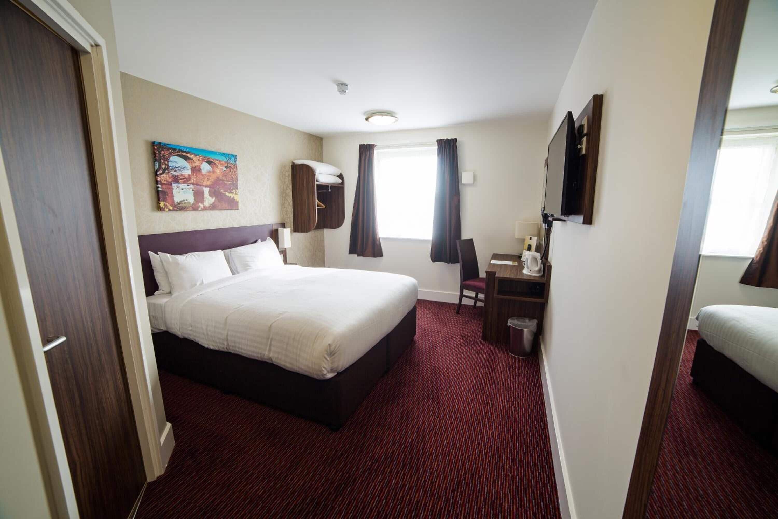 A hotel room with a large bed, a desk with a chair, and a window with curtains.