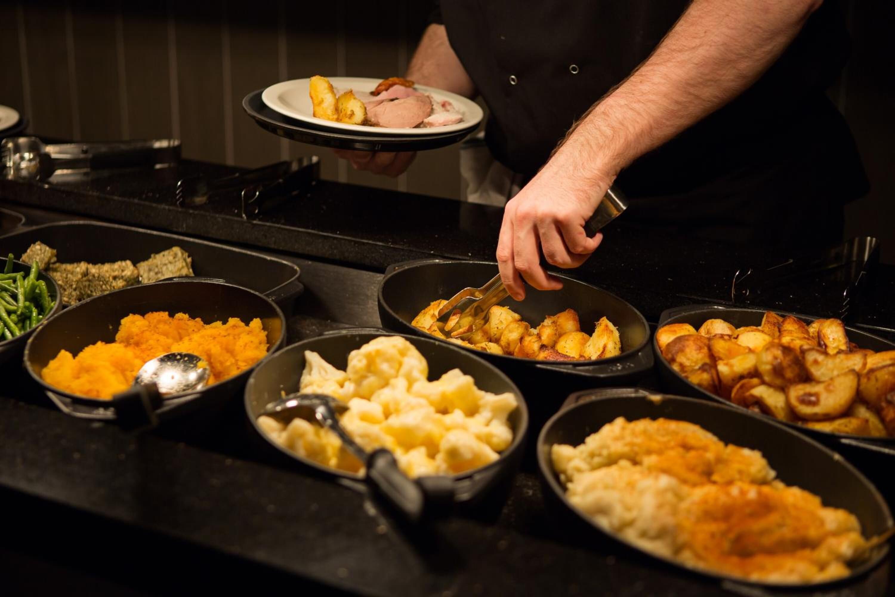 A buffet table with various dishes including mashed potatoes, roasted potatoes, and other prepared foods.