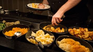 A buffet table with various dishes including mashed potatoes, roasted potatoes, and other prepared foods.