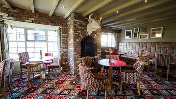 A cozy room with a brick fireplace, patterned carpet, and striped chairs.