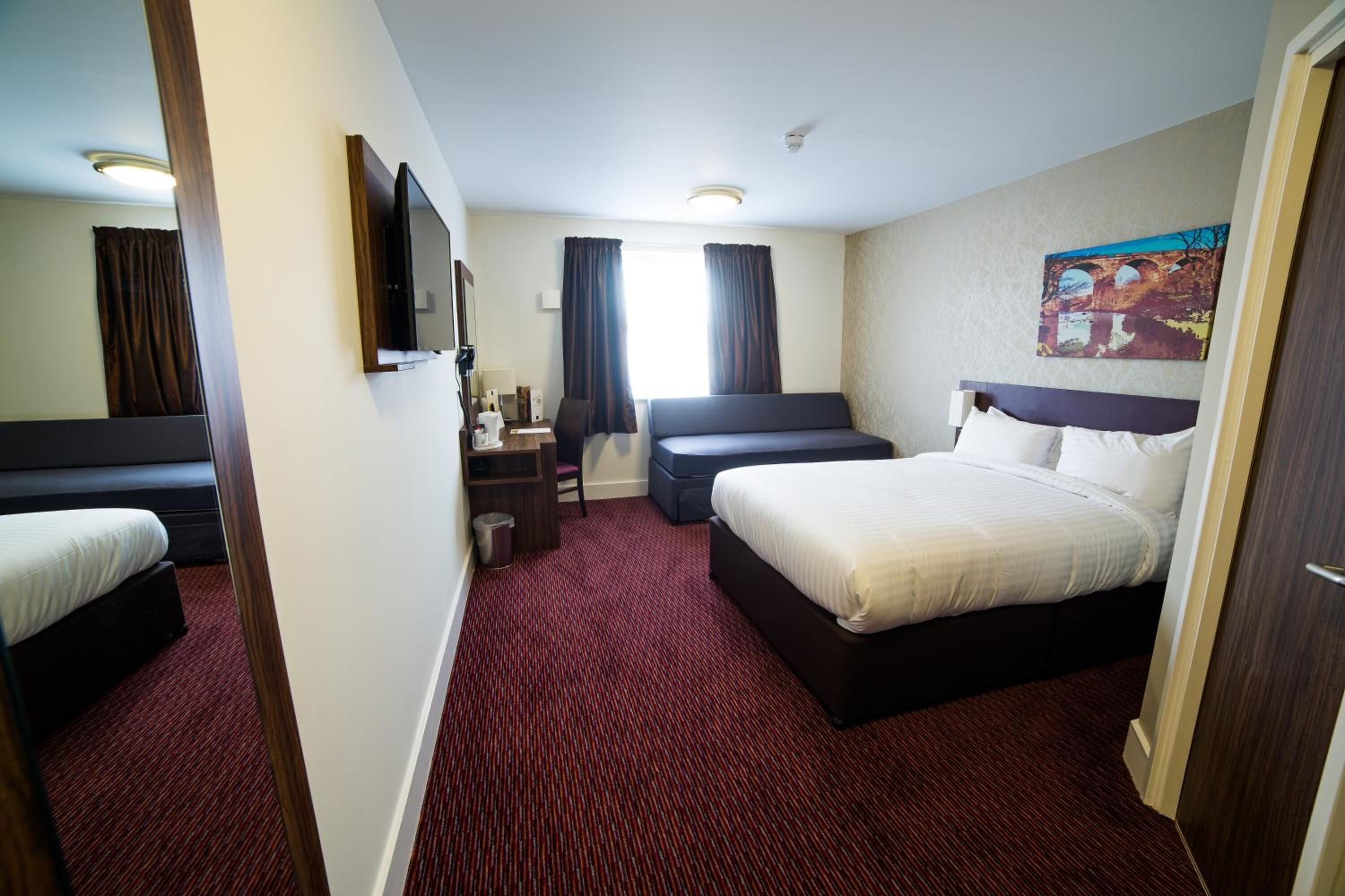 A hotel room with two beds, a desk, a chair, a TV, and a painting on the wall.