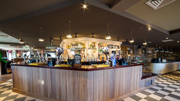 Un’area bar con pavimento a scacchi, bancone in legno e lampade a sospensione.