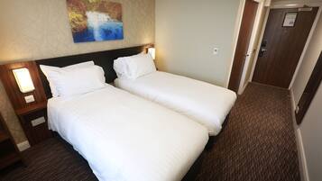 Een hotelkamer met twee eenpersoonsbedden, een nachtkastje met een lamp, een schilderij aan de muur en een vloerbedekking.
