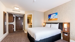 Una camera d'albergo con un letto grande, una testiera in legno, un quadro appeso al muro e un pavimento rivestito di moquette.