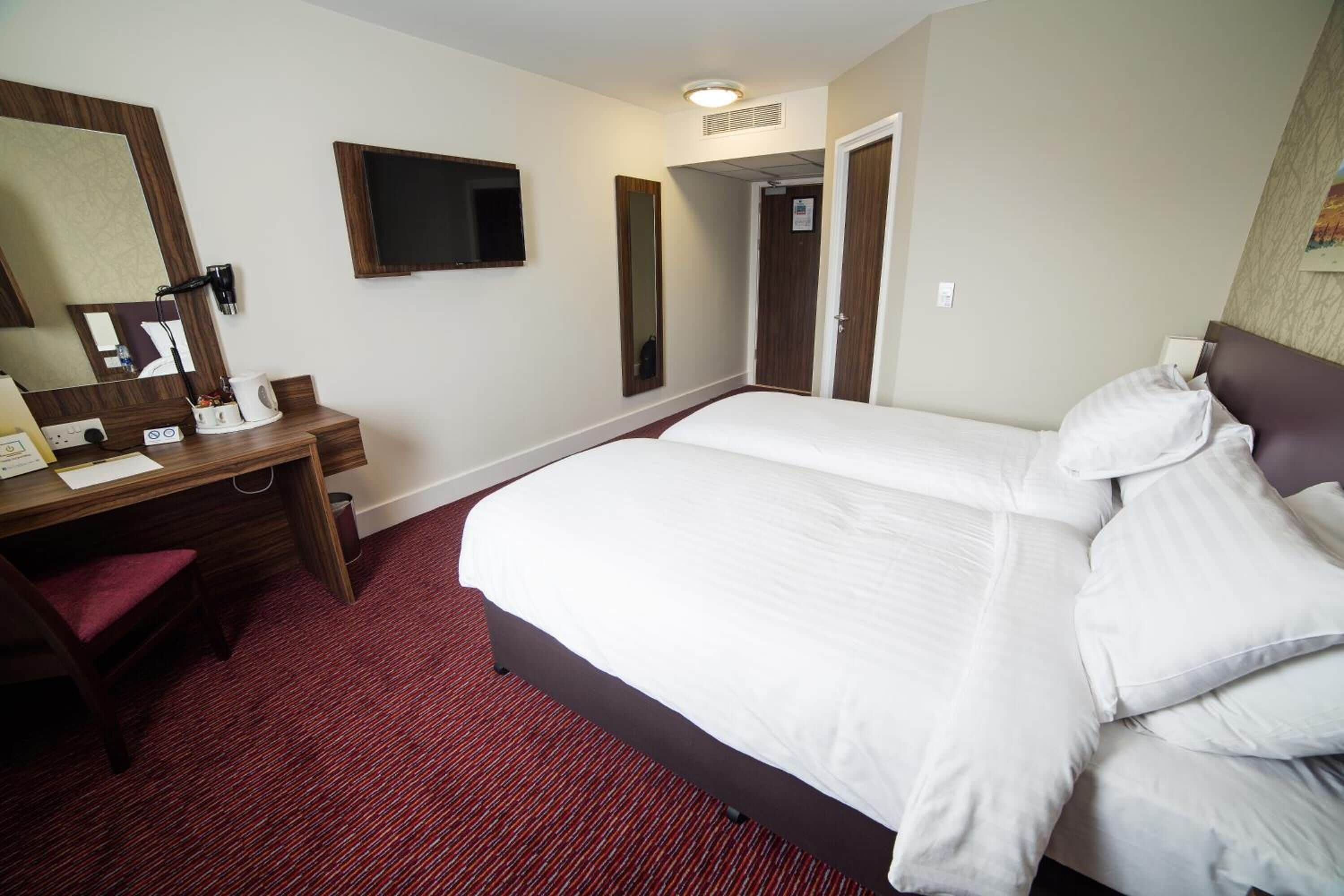 Habitación de hotel con una cama grande, un escritorio con silla, un espejo y una televisión.