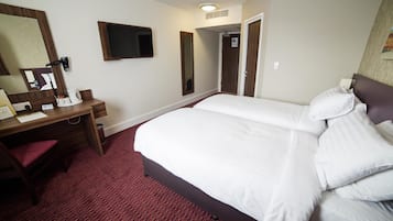 Habitación de hotel con una cama grande, un escritorio con silla, un espejo y una televisión.
