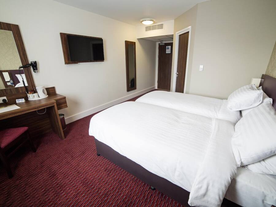 Habitación de hotel con una cama grande, un escritorio con silla, un espejo y una televisión.