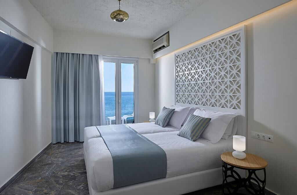 Habitación de hotel con cama, televisión, aire acondicionado instalado en la pared, panel decorativo y vista al mar.