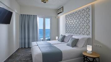 Habitación de hotel con cama, televisión, aire acondicionado instalado en la pared, panel decorativo y vista al mar.