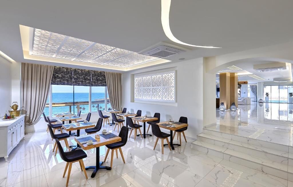 Un comedor moderno con mesas y sillas, vista al mar y un techo decorativo.