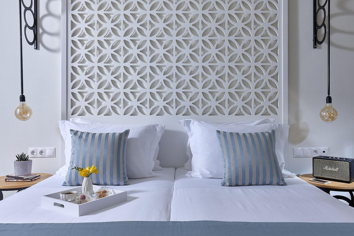 A neatly arranged hotel room with a bed, pillows, a bedside table, a radio, and a decorative wall panel.