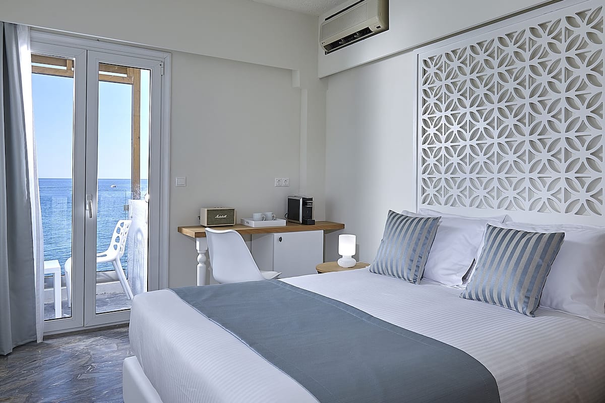 Een hotelkamer met een bed, een bureau, een stoel en uitzicht op zee.