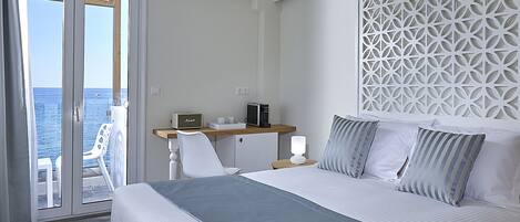A hotel room with a bed, a desk, a chair, and a view of the sea.