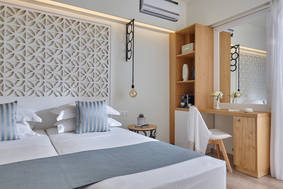 Een moderne hotelkamer met een groot bed, een bureau en een spiegel. Er is een decoratief wandpaneel en een klein tafeltje met een plant.