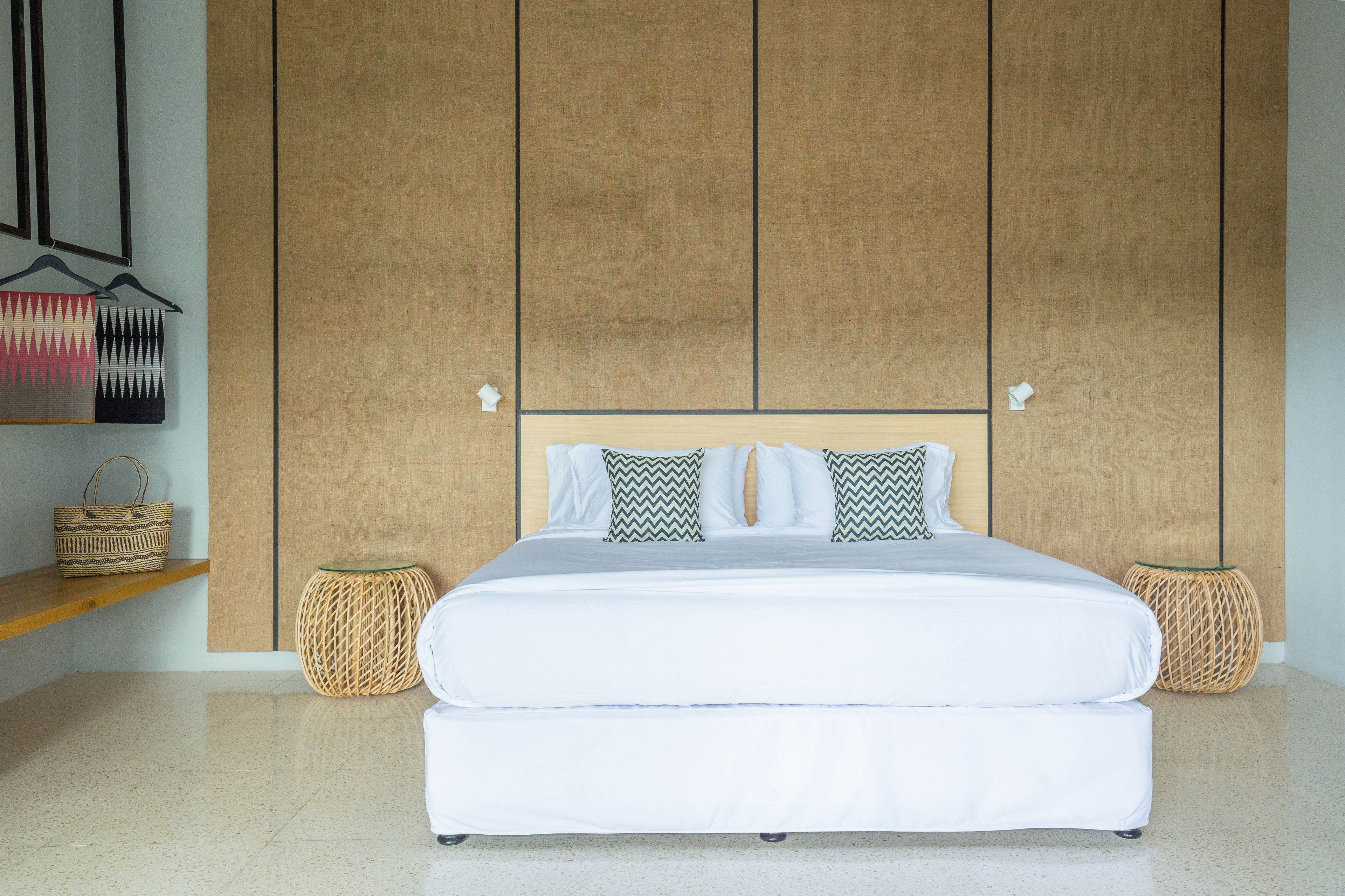 A neatly arranged bedroom with a large bed, two side tables, a hanging basket, and a wooden panel wall.