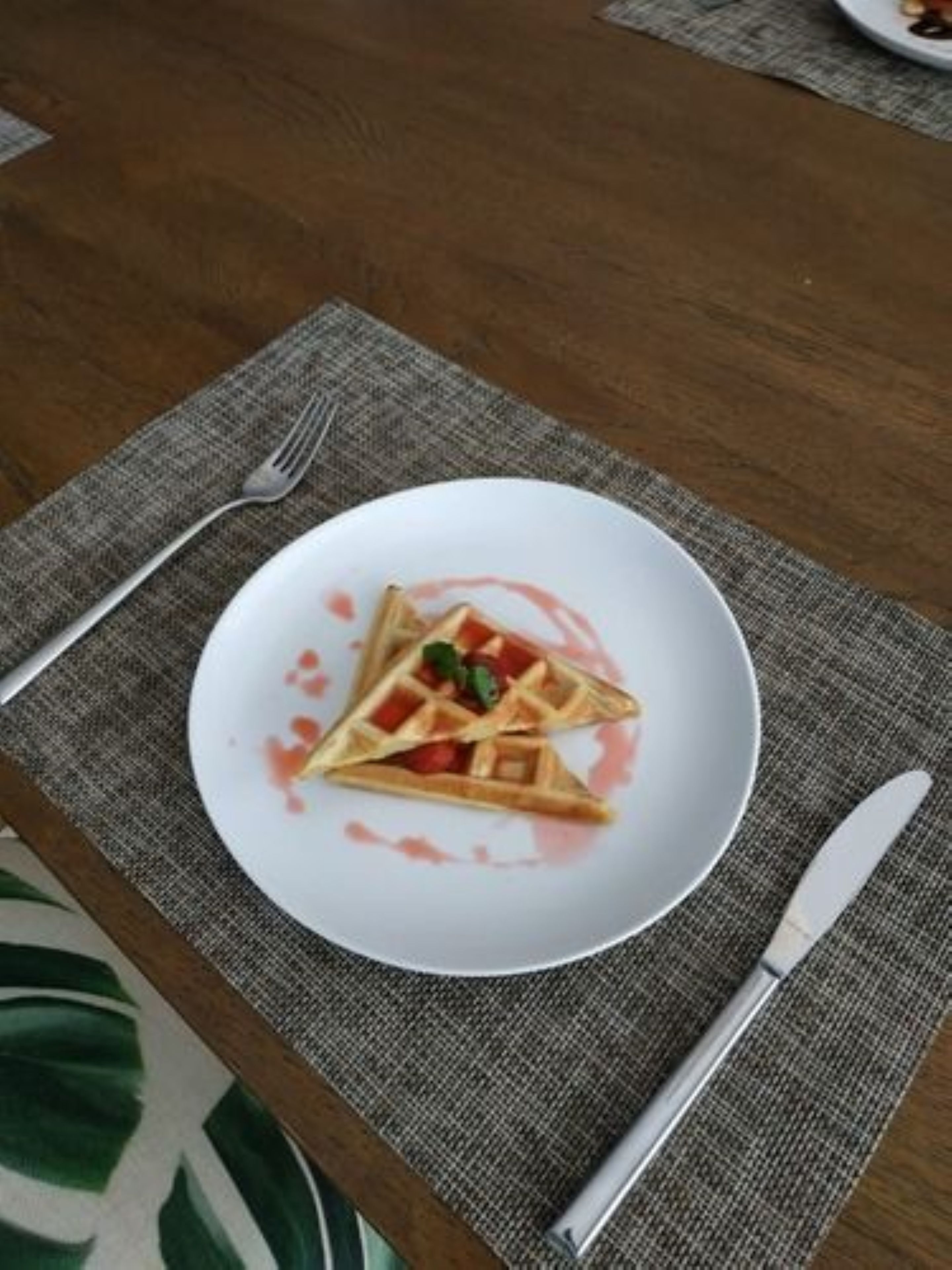A plate of waffles with syrup and a small green garnish on a white plate, placed on a table with a gray placemat.