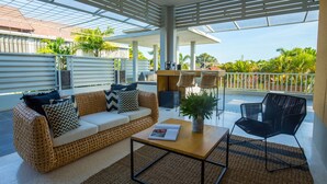 Un balcon spacieux avec un canapé en osier, une table basse et une chaise noire.