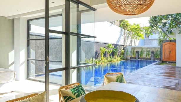 Un espace extérieur moderne doté d’une porte vitrée donnant accès à une zone piscine, entourée de mobilier en bois et d’un luminaire suspendu en osier.