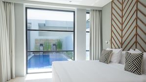 Une chambre d’hôtel moderne avec un grand lit, une vue sur une piscine et un mur orné d’un motif en chevrons.