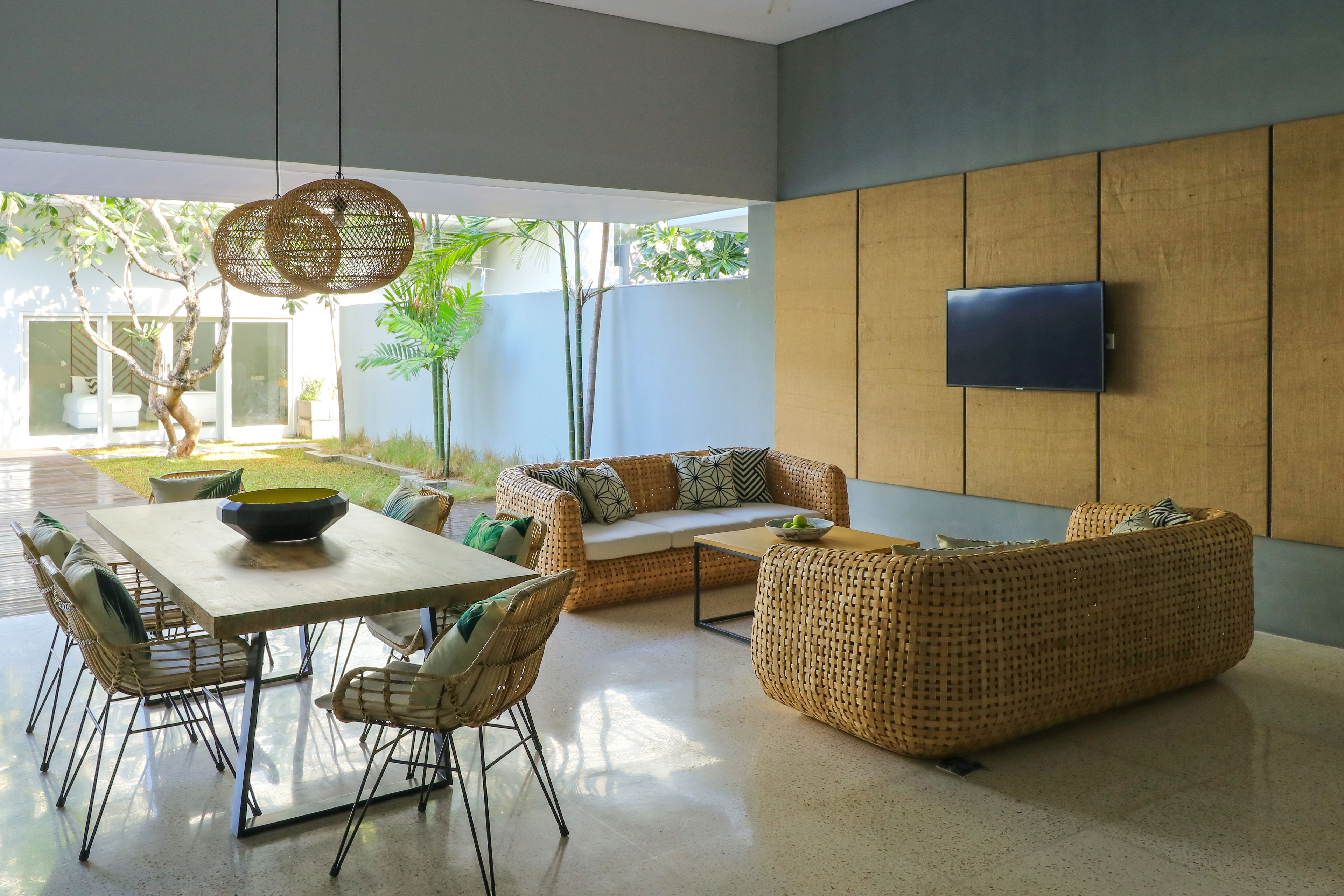 A modern living room with a sofa, dining table, chairs, and a TV mounted on the wall.