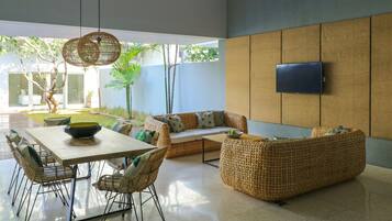 A modern living room with a sofa, dining table, chairs, and a TV mounted on the wall.