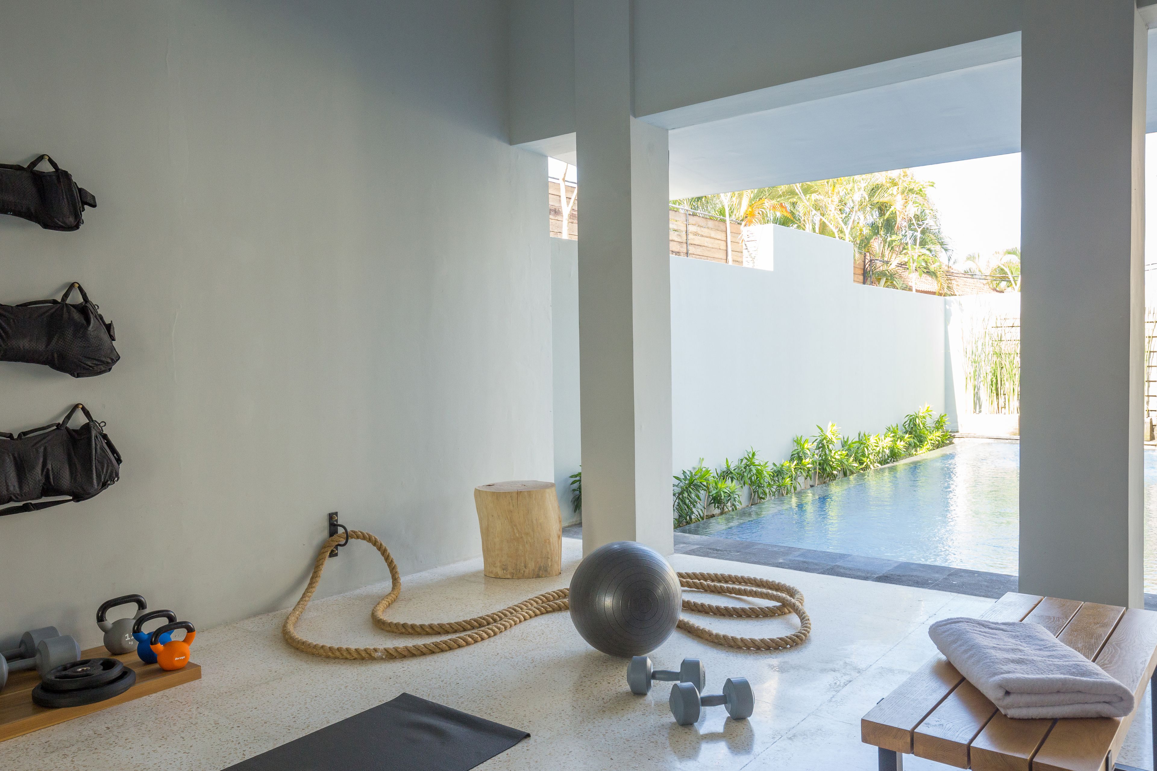 Un gimnasio con equipo de ejercicio, un banco de madera y vista a una piscina exterior.