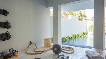 Un gimnasio con equipo de ejercicio, un banco de madera y vista a una piscina exterior.