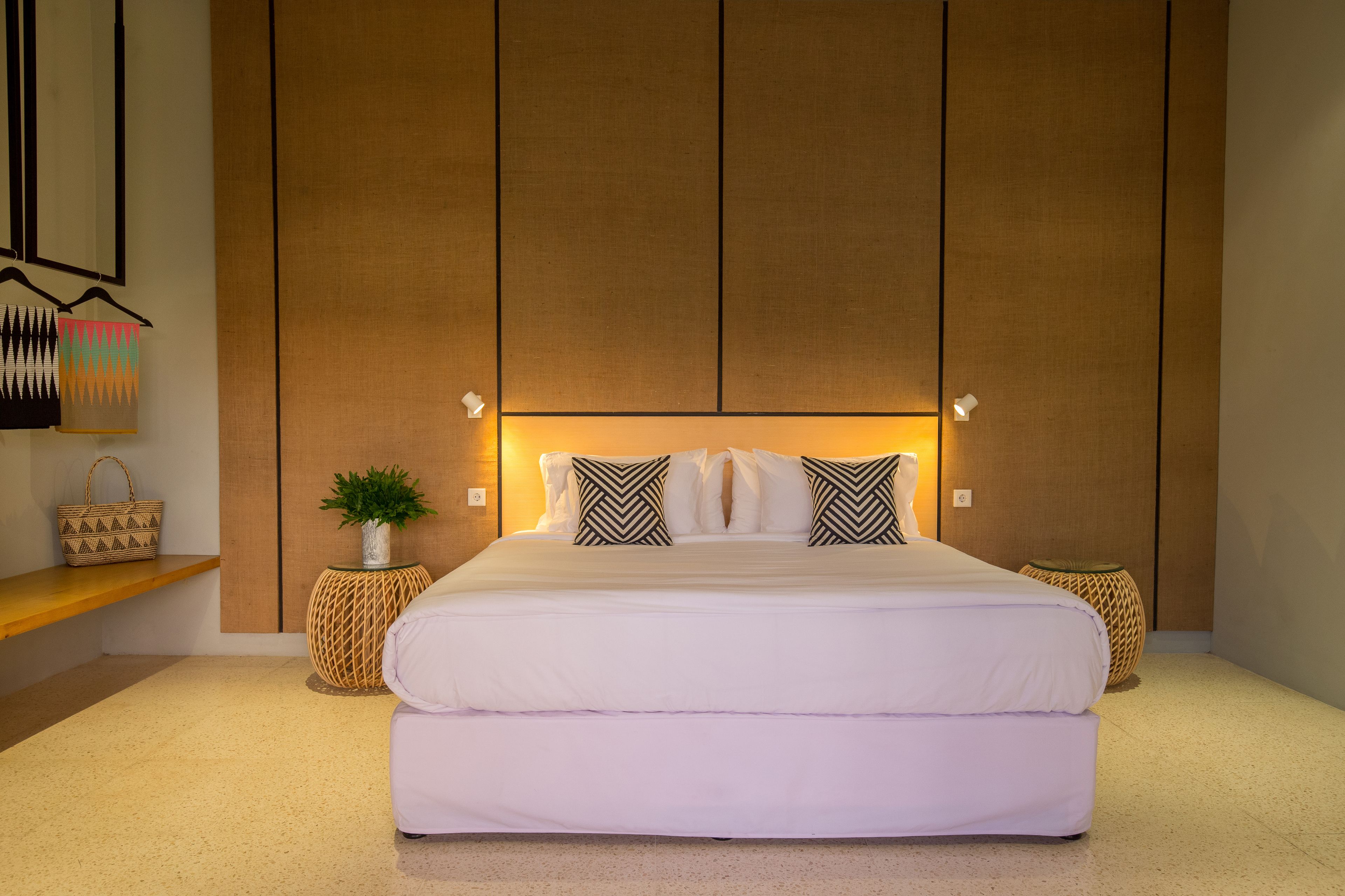 A modern bedroom with a large bed, two bedside tables, a wall-mounted shelf, and a decorative wall hanging.
