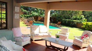 Un patio abrité avec des meubles blancs, une piscine et un jardin luxuriant.