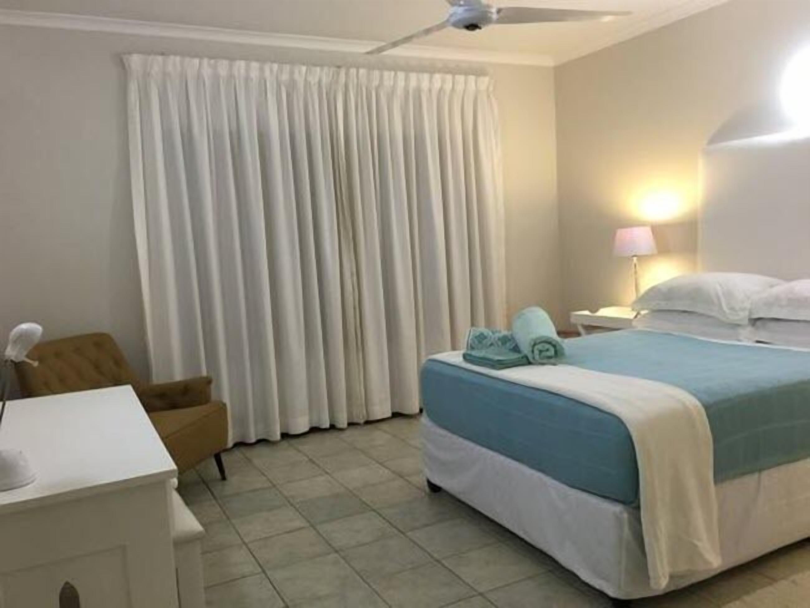 A hotel room with a bed, a chair, a desk, and a curtain.