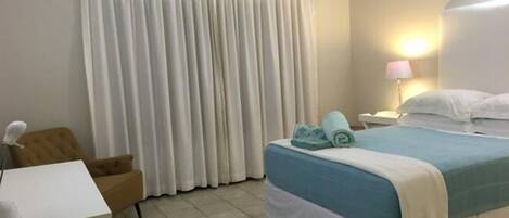 A hotel room with a bed, a chair, a desk, and a curtain.