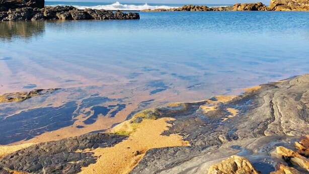 Un rivage rocheux bordé d’une eau d’un bleu limpide, avec un bateau visible au loin.