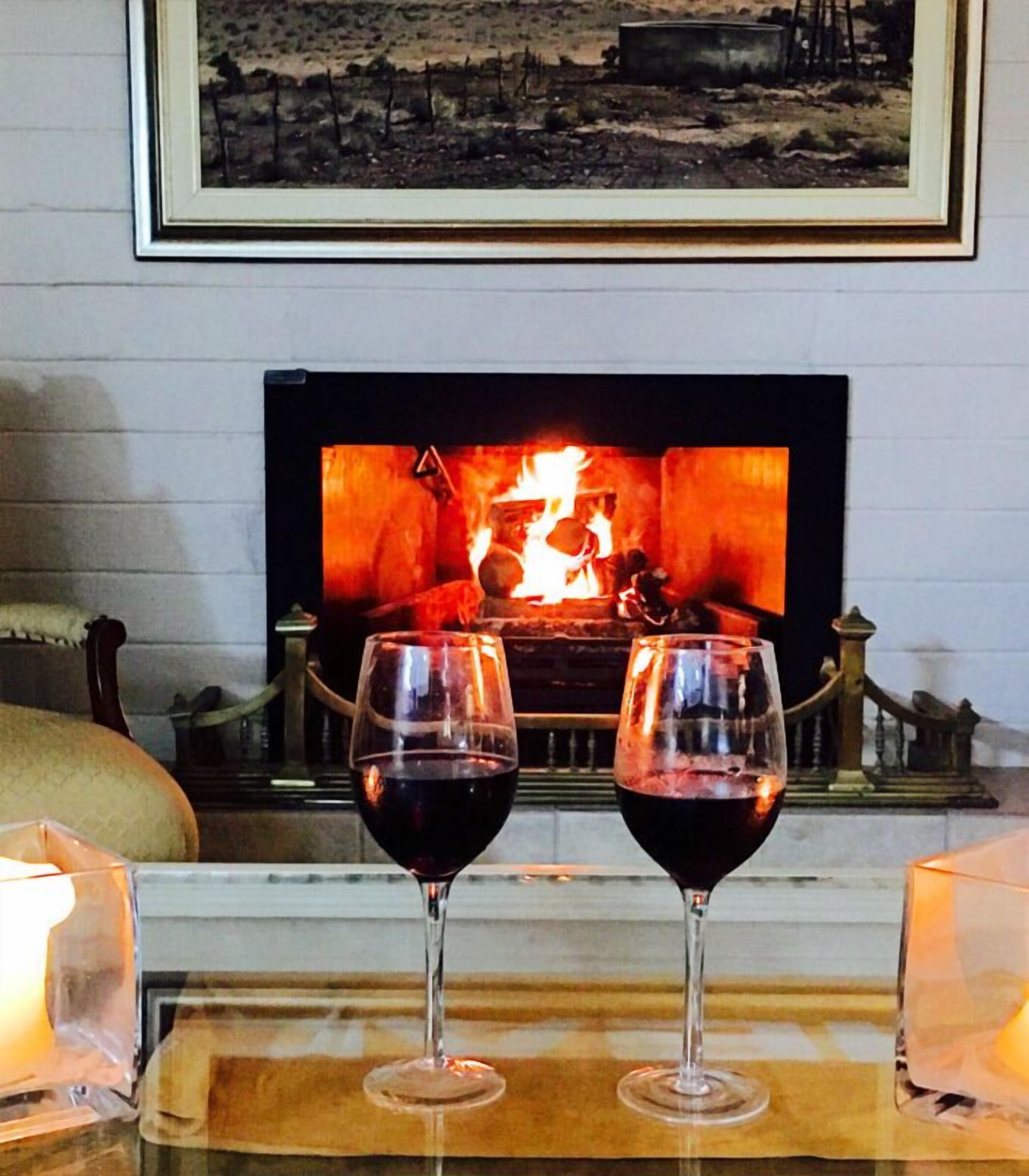 Dos copas de vino sobre una bandeja frente a una chimenea encendida.