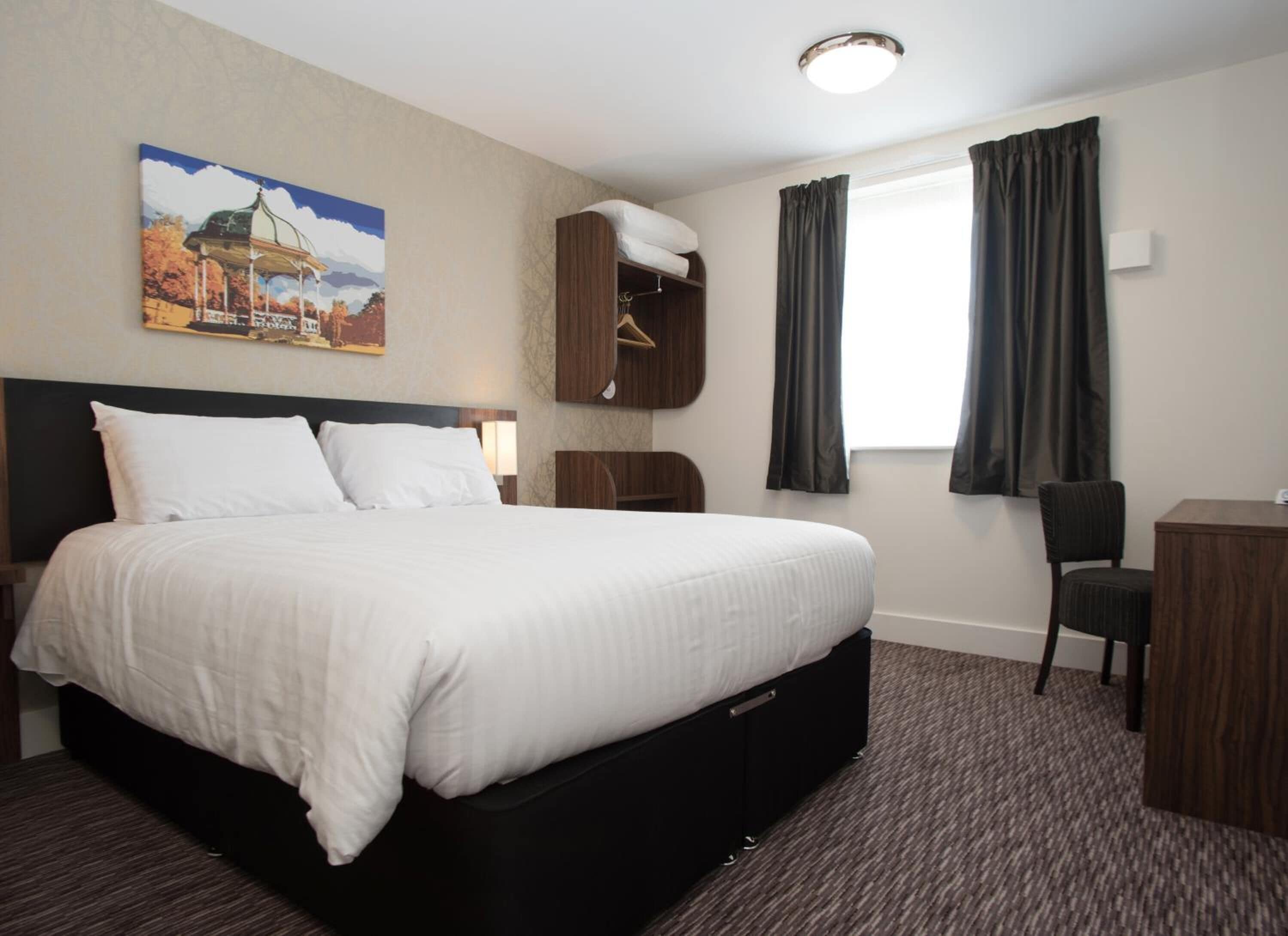 A hotel room with a large bed, a desk, a chair, and a wardrobe.