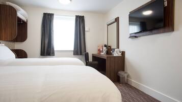 A hotel room with two beds, a desk, a mirror, a television, and a window with curtains.