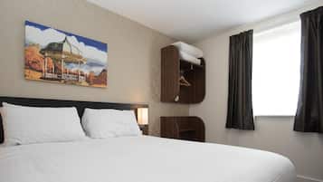 A hotel room with a large bed, a wooden wardrobe, a painting of a gazebo, and a window with curtains.