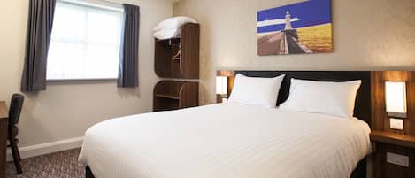 Una habitación de hotel con una cama grande, una mesita de noche, una silla, un armario y un cuadro de un faro.