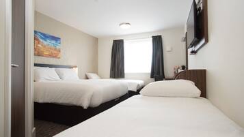 Una habitación de hotel con dos camas, un cuadro en la pared, una ventana con cortinas y un televisor de pantalla plana montado en la pared.