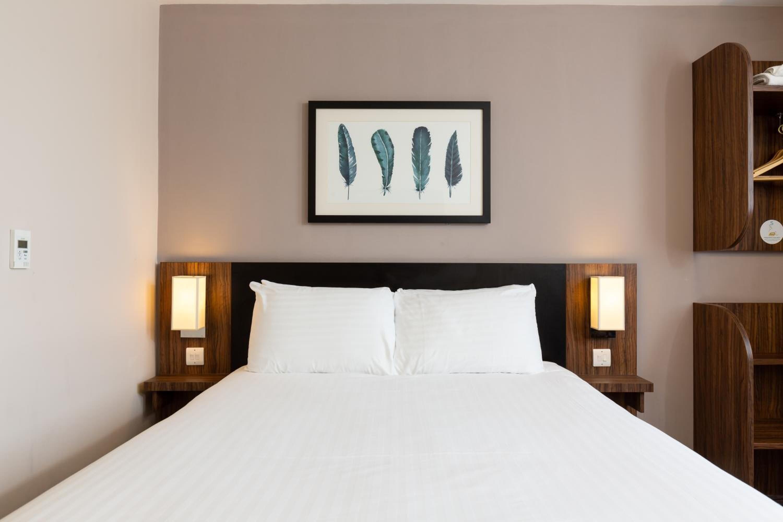Hotelkamer met een groot bed, twee bedlampen, een lijst met een afbeelding van veren en een houten nachtkastje met een plank.