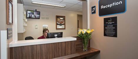 A reception desk with a wooden finish, a computer, and a vase with yellow flowers.