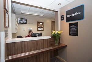 A reception desk with a wooden finish, a computer, and a vase with yellow flowers.