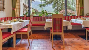 A dining area with red cushioned benches and white tables, overlooking a scenic mountainous landscape. - Pension Sunnhofer (Terlano)