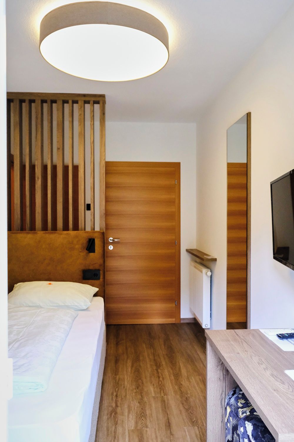 A hotel room with a bed, a wooden headboard, a door, a mirror, and a television.
